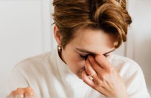A close-up shot of a woman rubbing her eyes, conveying stress and fatigue indoors.