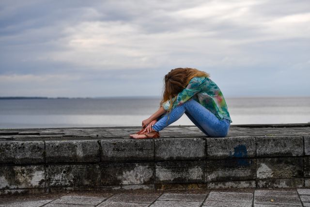 A young woman sitting on a stone wall by the sea, embracing a serene summer atmosphere.
